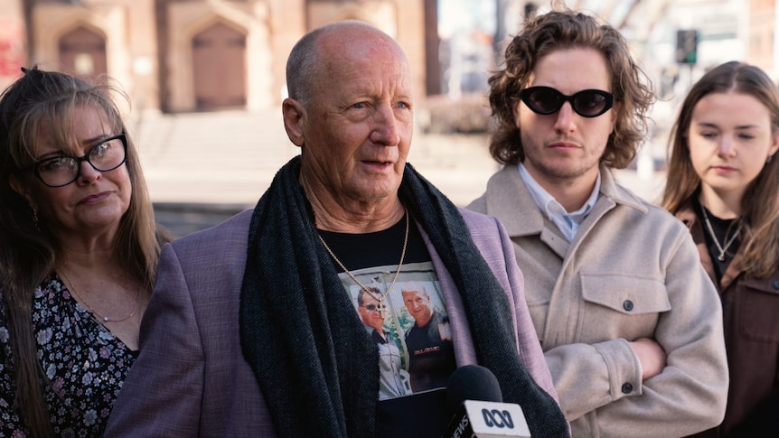 A bald man speaking into an ABC microphone outside of court with his family