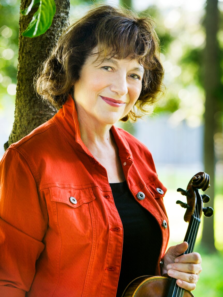 Violist and teacher Patricia Pollett in a red coat, holding her viola in her left hand.