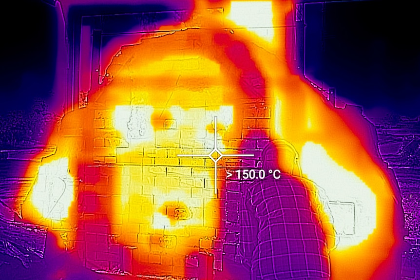 A thermal image showing a temperature of 150 degrees C on the outside of a kiln as a woman leans toward it.