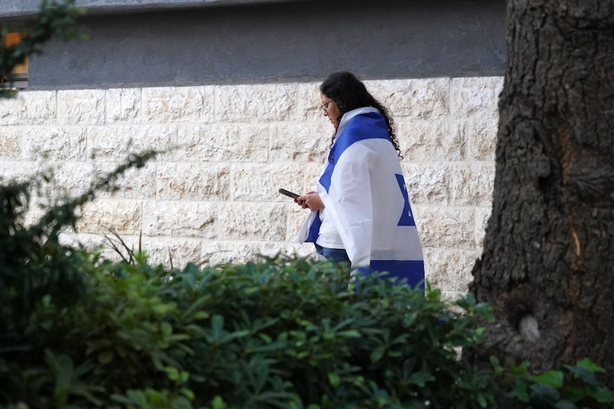 A woman with a flag draped over her shoulders, looking at her phone, seen from a distance
