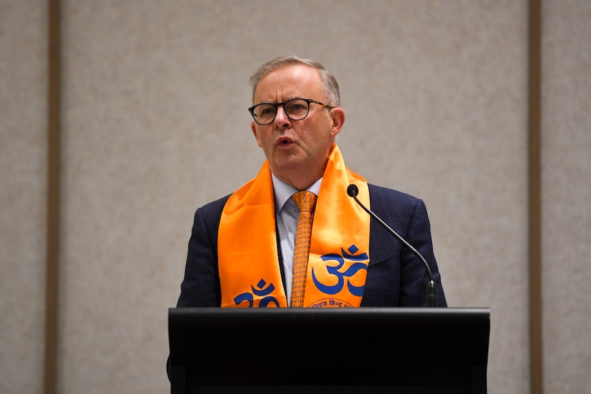 Anthony Albanese gives a speech while wearing an orange scarf over his shoulders. 