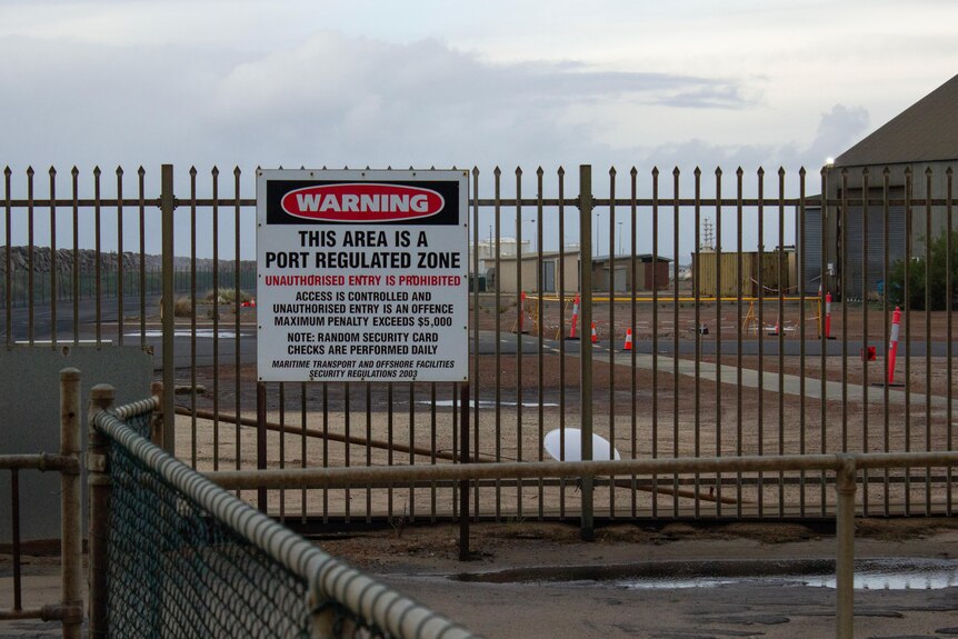 A sign on a fence reads 'WARNING This area is a port-regulated zone'