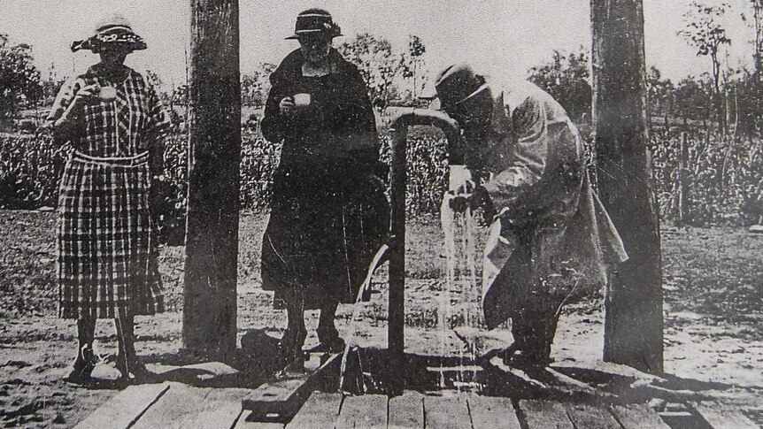B&W image of three people pouring spa water from a hand pump