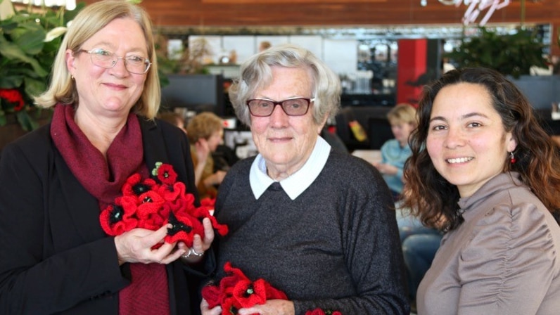 Three women hold knitted red poppies in their hands.