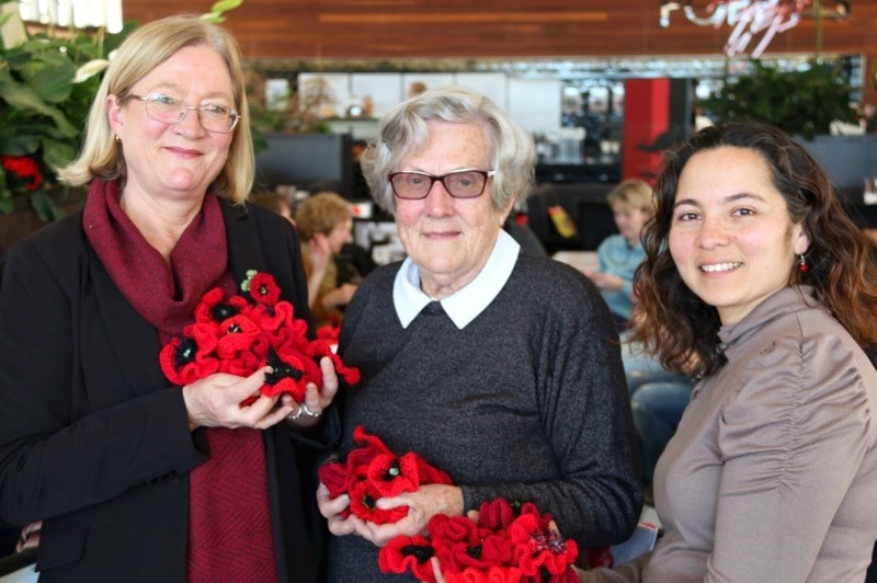 Three women hold knitted red poppies in their hands.