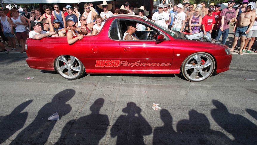 Visitors look on as a car drives by on Tuff Street at the Summernats festival in Canberra.
