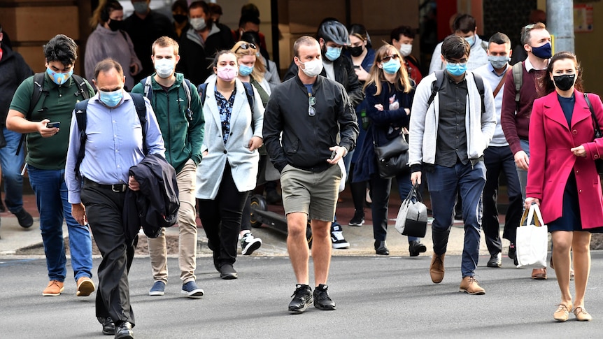 在布里斯班中央商务区，一群戴着口罩的人穿过一个交叉路口。