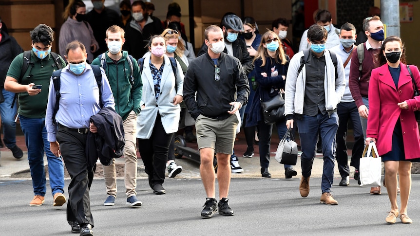 Crowd of people wearing face masks walking across a scramble crossing in Brisbane CBD.