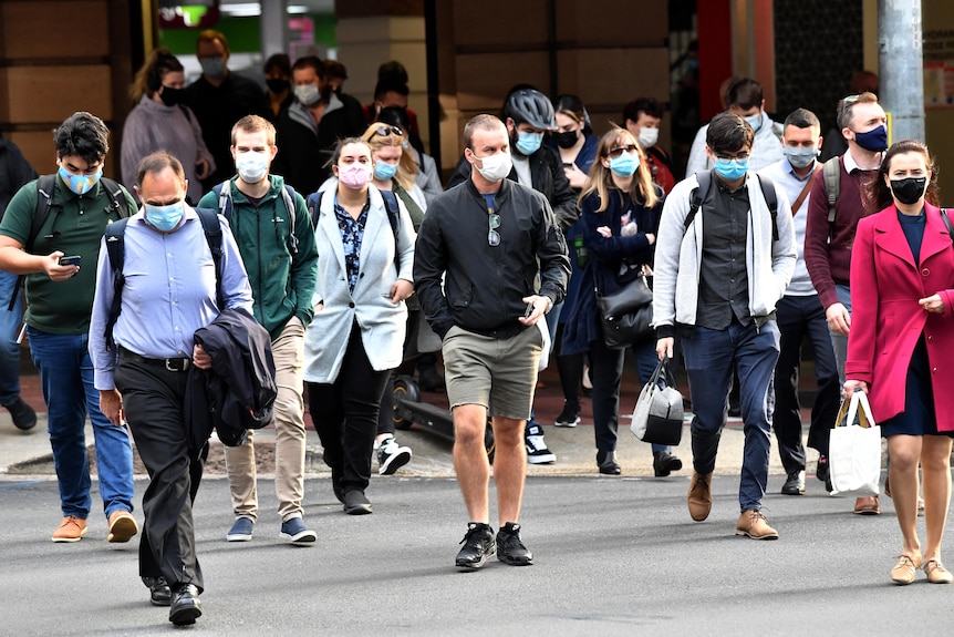 A crowd of people wearing face masks walk across a scramble crossing in Brisbane CBD.