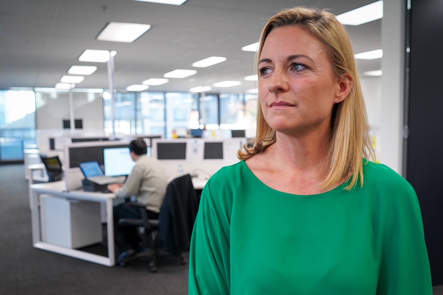 A woman in a green top stands in an office.