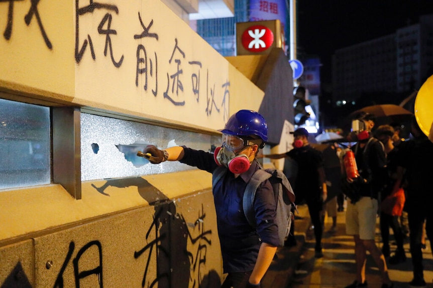 A protester smashes a window at train station entrance during a protest in Mong Kok, Hong Kong, which has graffiti over it.