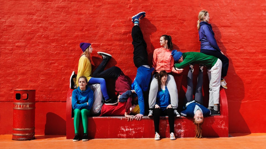 Young people sitting and lying on each other on a red bench