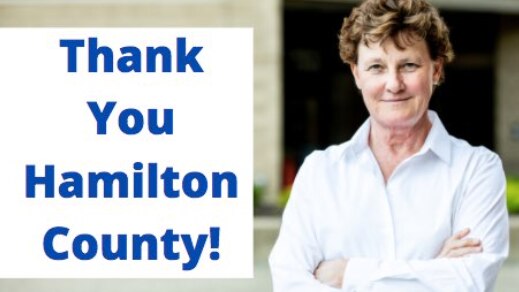 Woman stands smiling with arms crossed next to sign saying thank you Hamilton County.