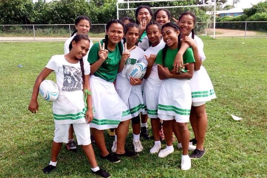 Medium shot of a group of girls posing for the camera on a playing field.