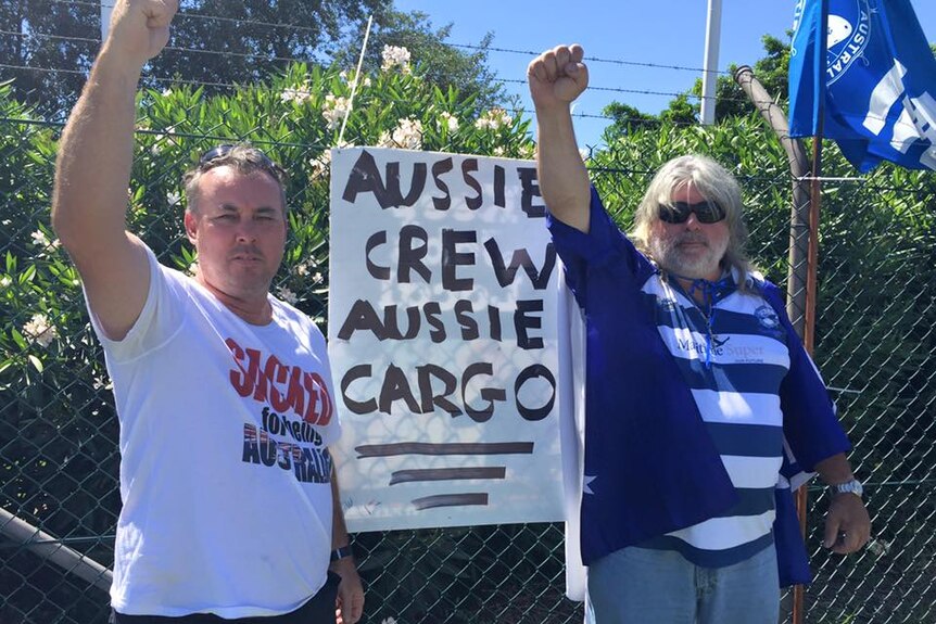 Two men stand with their arms up in front of a sign that says 'Aussie Crew, Aussie Cargo'.