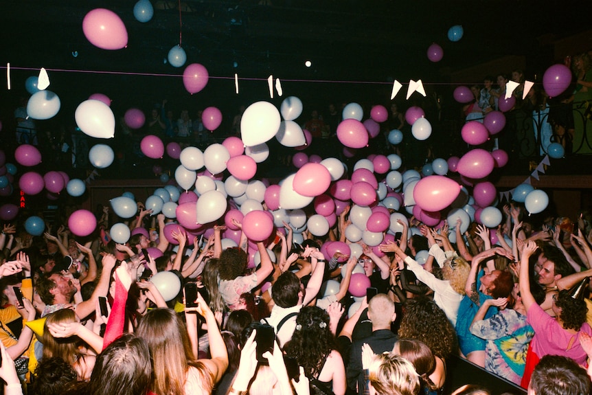 A sea of people are seen dancing in the Tivoli, with a flash illuminating the crowd as pink and white balloons drop from above.