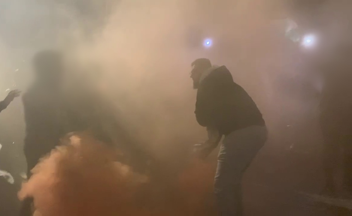 a man wearing a hooded jumper can be seen through the mists of orange flare smoke at the Sydney Opera House
