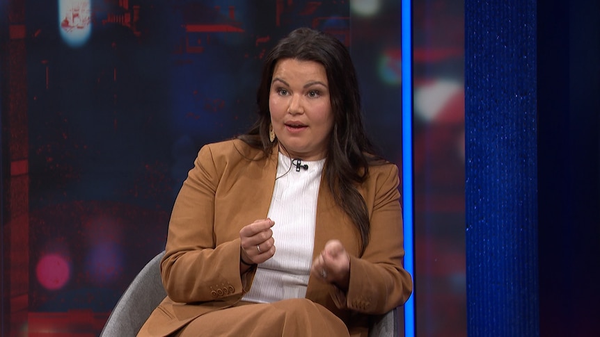 A young Aboriginal woman in a tan suit gestures while speaking on the Q+A set.