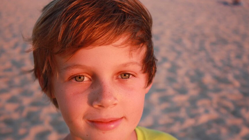 Sunset glow lights up the face of a 12-year-old boy standing on a beach for a portrait photo