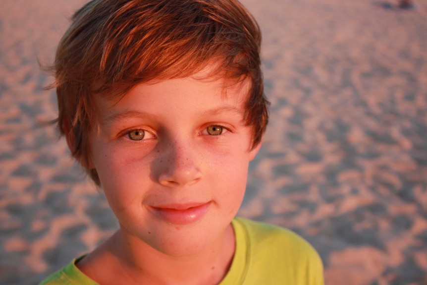 Sunset glow lights up the face of a 12-year-old boy standing on a beach for a portrait photo