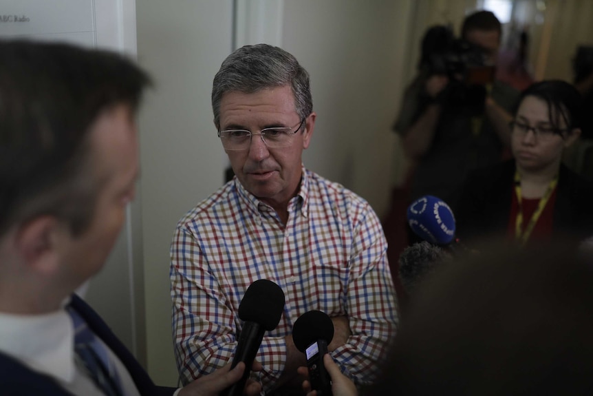 David Gillespie stands in a corridor surrounded by cameras and journalists