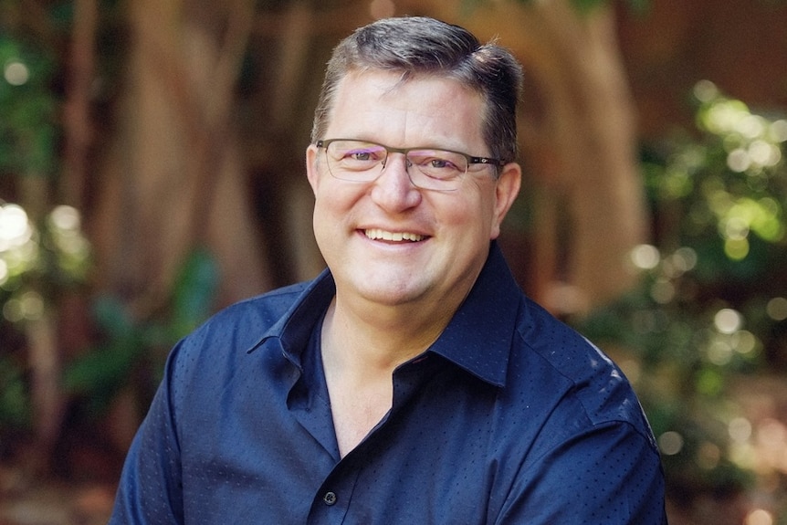 A man smiling as he stands in front of a large tree