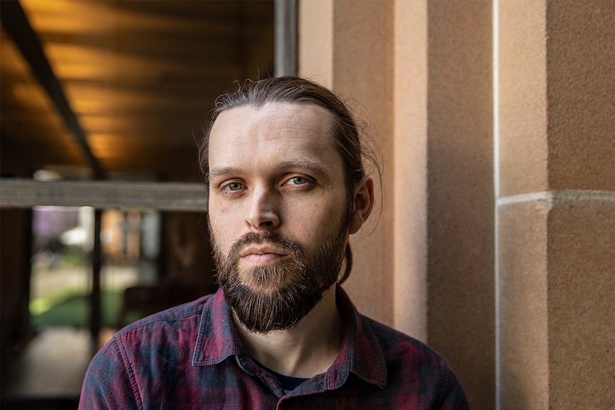 Colour photo of artist Andrew Tenison standing in front of sandstone exterior and window at the Museum of Contemporary Art.