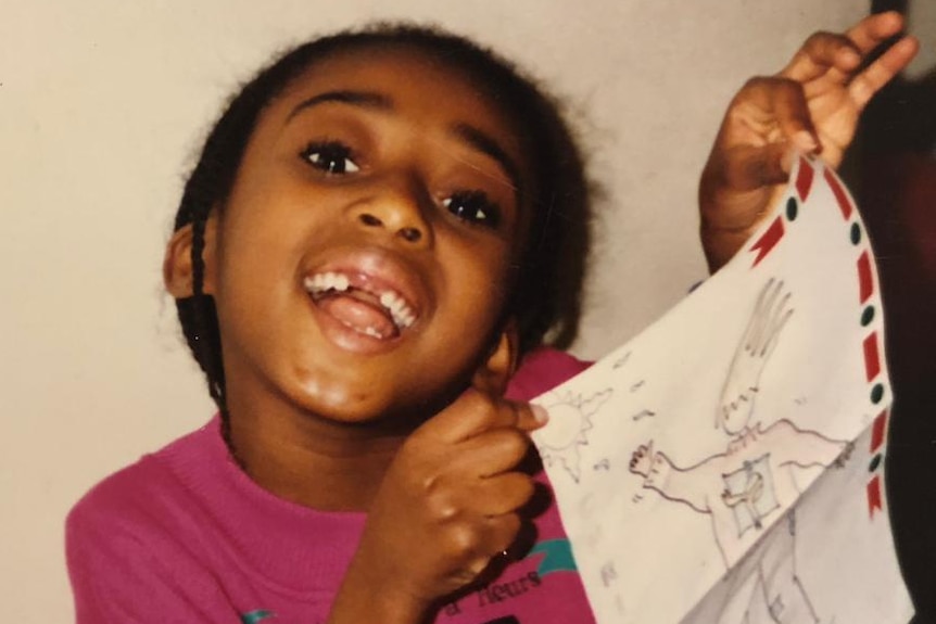 A girl missing her two front teeth holds up her drawing
