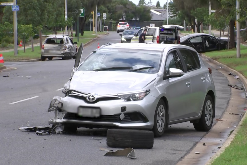 A road with three damaged cars and an ambulance in the background