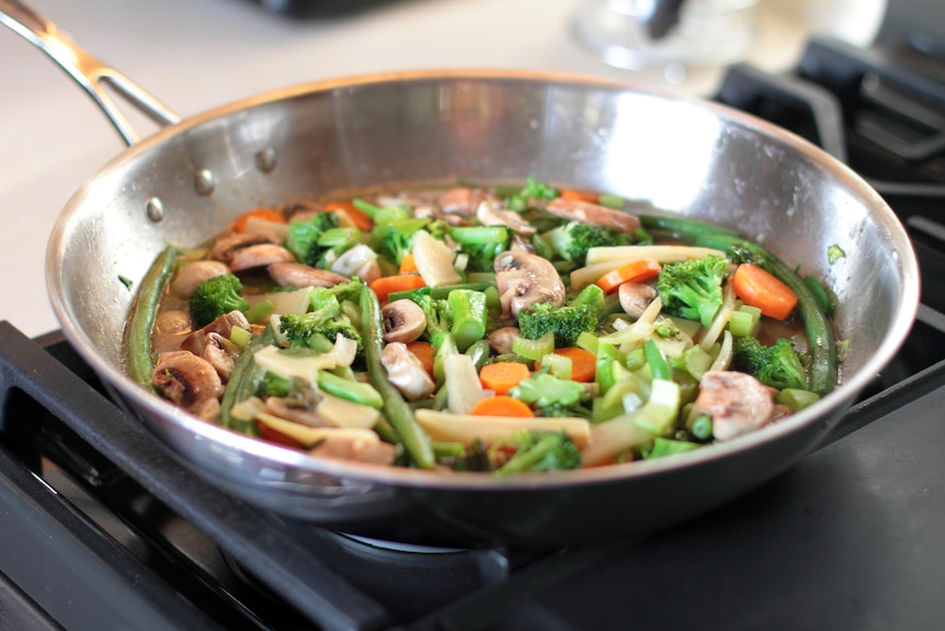 a bright coloured stirfry cooking in a stainless steel pan