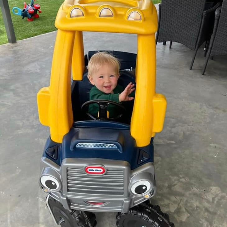A blonde boy smiling at the family sitting in a large yellow toy car with eyes