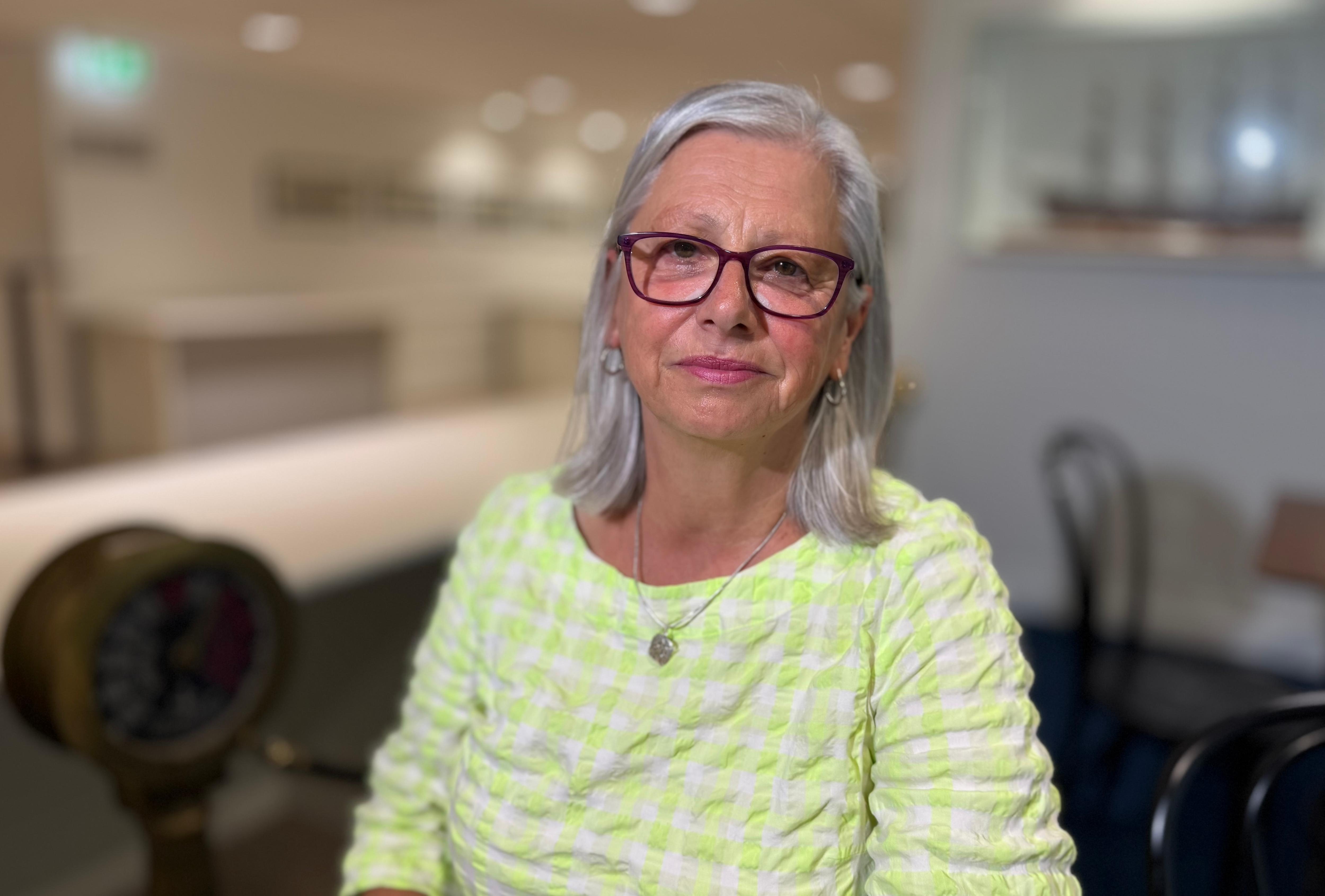 A woman with glasses and a green shirt looking at the camera
