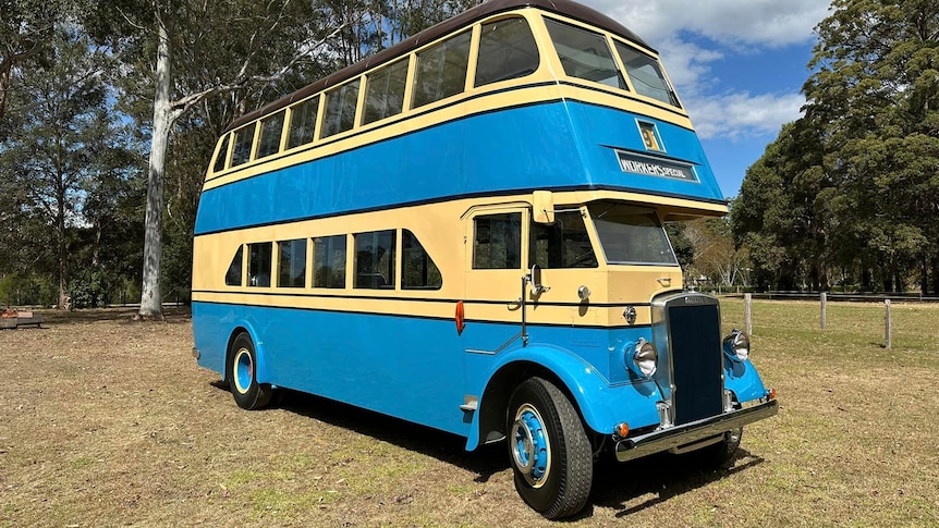 The blue and cream double decker bus is parked outside in a large grassed area.