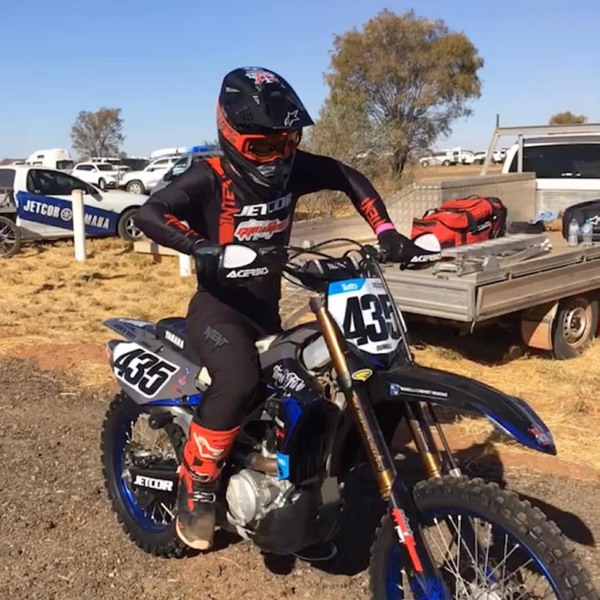 A man in safety gear on dirt bike in a desert town.