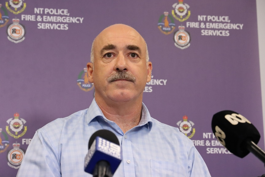 A male NT Police officer standing before several microphones, in front of a NT Police banner.