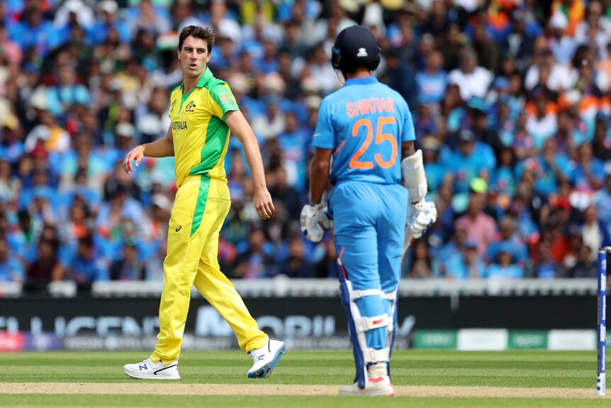 Pat Cummins, wearing yellow cricket kit, lets out a sigh as Shikhar Dharwan, wearing blue, looks on