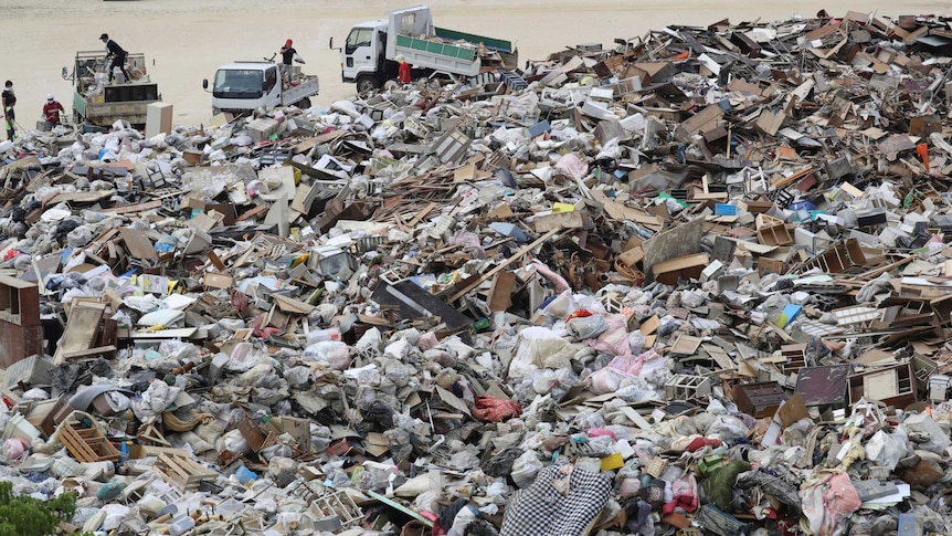 Men in trucks dump rubbish and debris in a huge pile