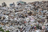 Men in trucks dump rubbish and debris in a huge pile