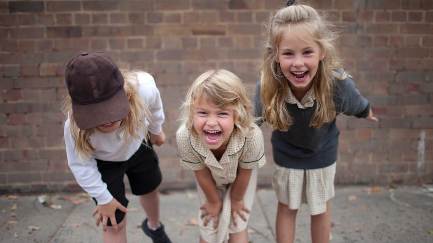 three school children smiling at the camera in their uniforms