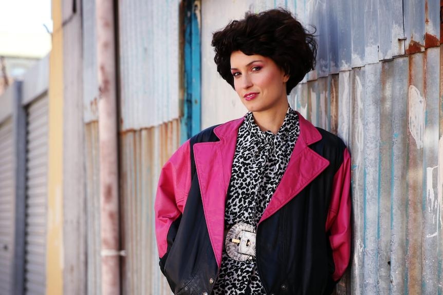 Missy Higgins, styled in 80s hot pink fashion, stands in an alleyway
