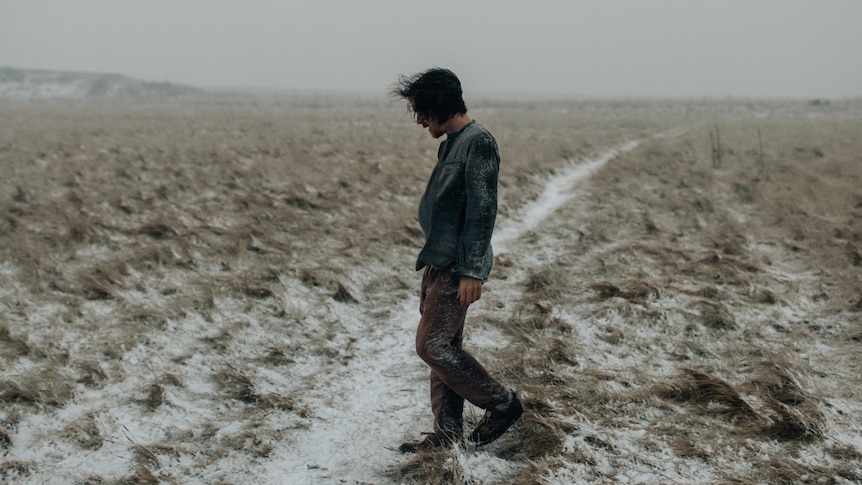 Damien Rice walks through a snow-blasted field, wind blowing his hair
