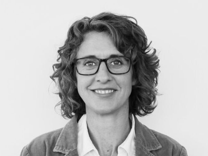 A black and white photo of a lady with brown curly hair and glasses smiling at the camera in a professional portrait shot