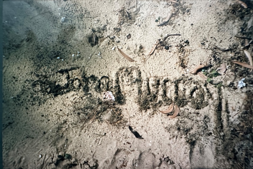 the name John Murray scratched into sand