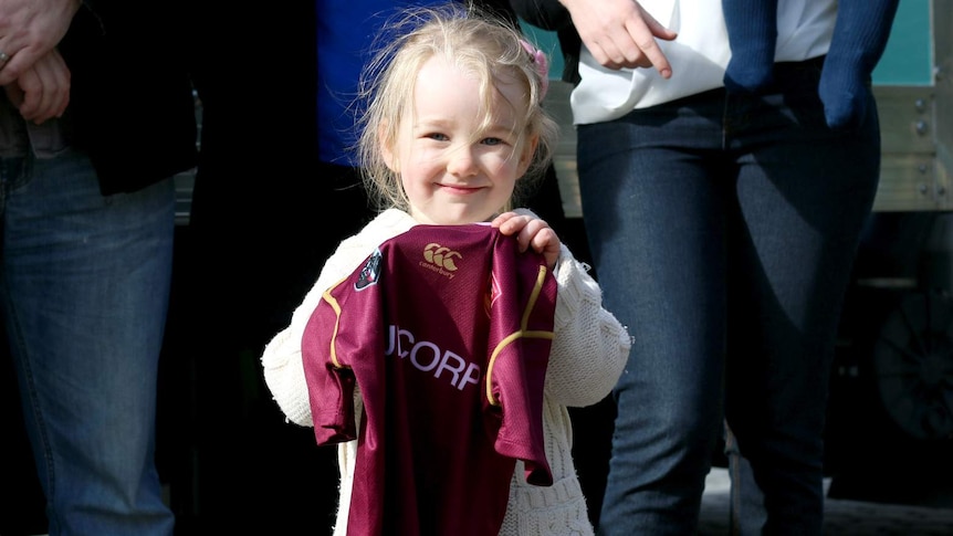 A little girl holding a football jersey.