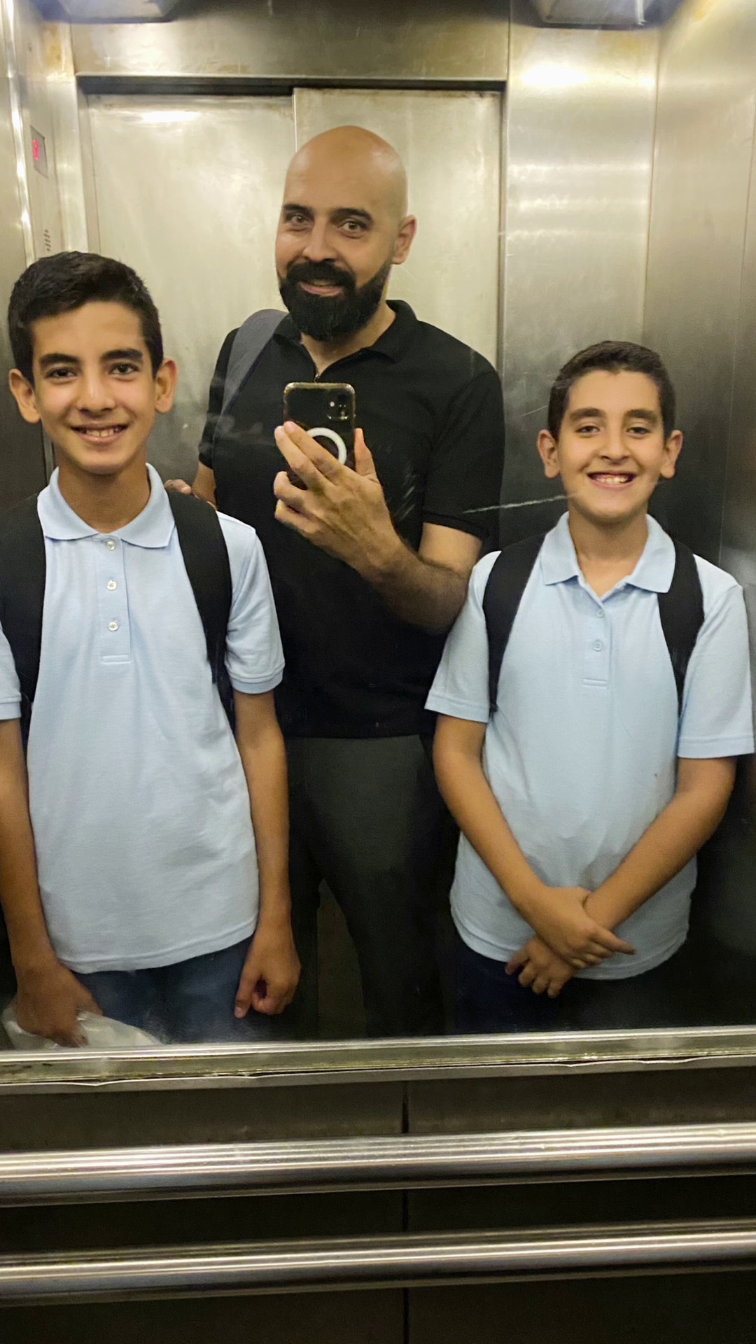 Man in a lift with his two sons in school uniform, taking a photo in front of the mirror. 