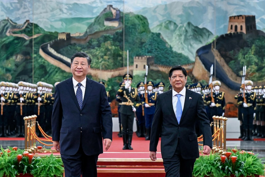 Two men in suits stand before a military honour guard and a painted backdrop showing the Great Wall of China.
