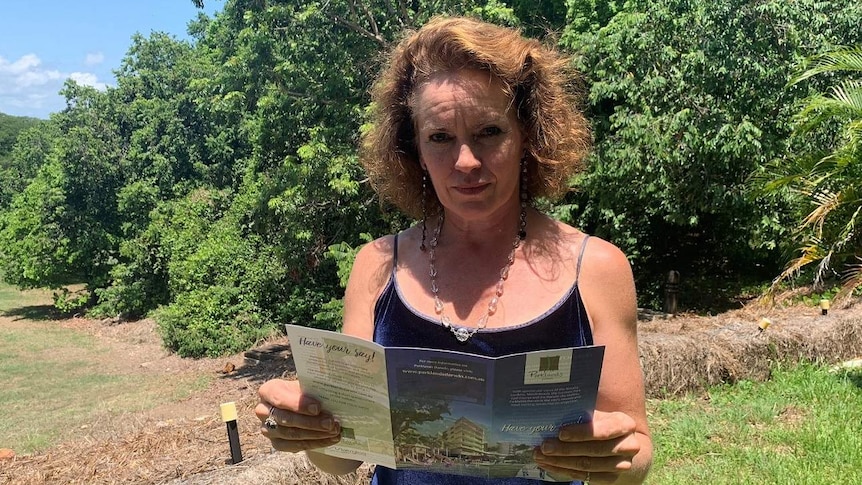 Catherine McAlphine stands at the site of a planned development with a brochure.