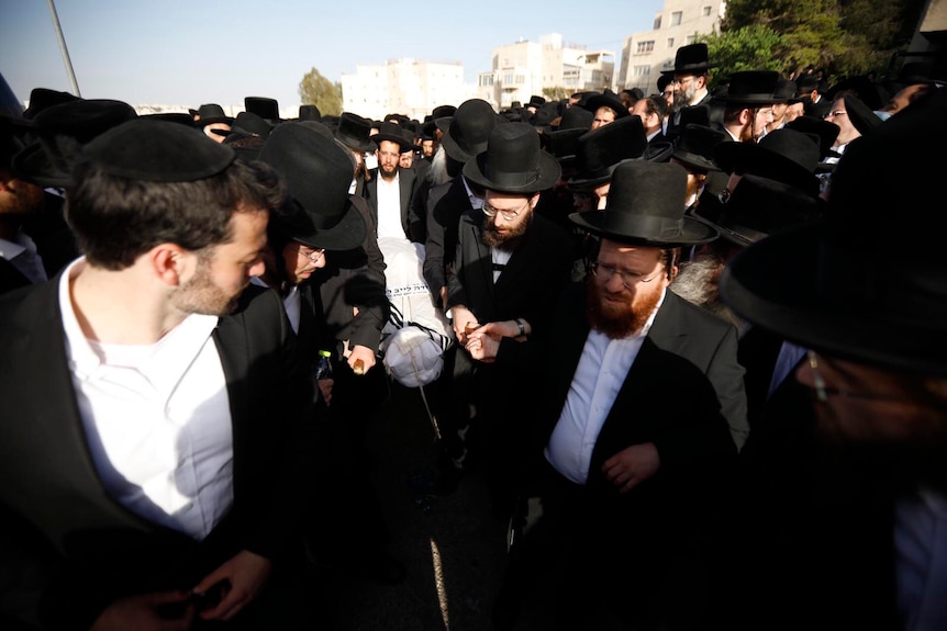 Mourners in black suits carry a body wrapped in white cloth.