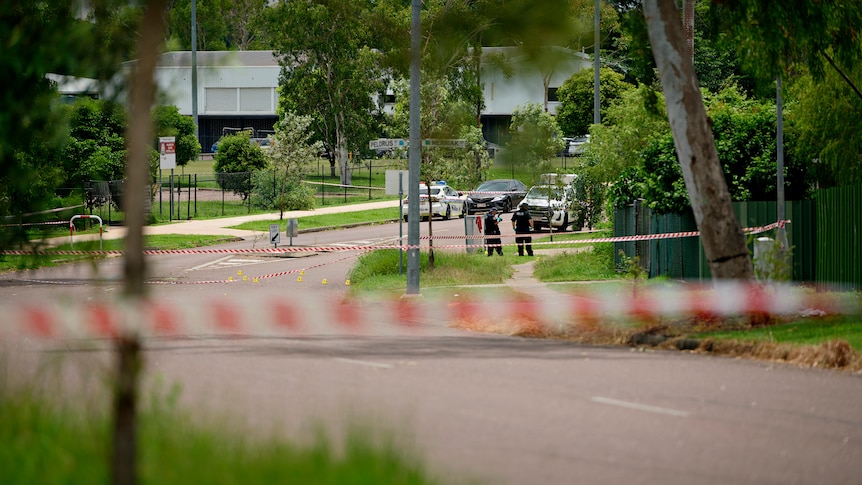 A police tape blocks off a suburban street. Police can be seen in the background talking.