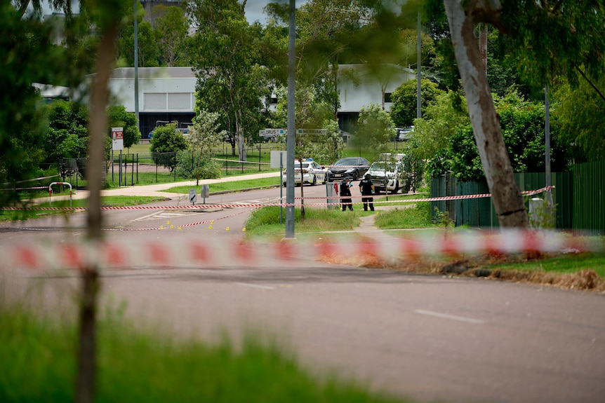 A police tape blocks off a suburban street. Police can be seen in the background talking.